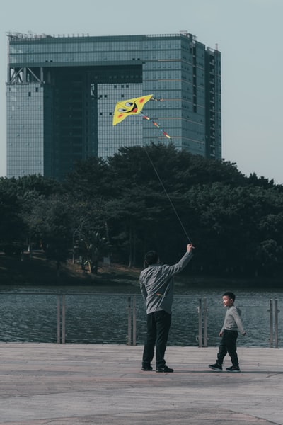 一个穿着白色长袖衬衫和灰色裤子的男人白天在湖边钓鱼